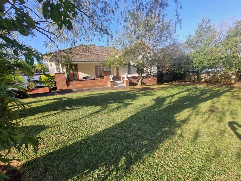 A front view of a single-story house featuring a tiled roof, brick facade, and a covered porch, set within a spacious, well-maintained garden.