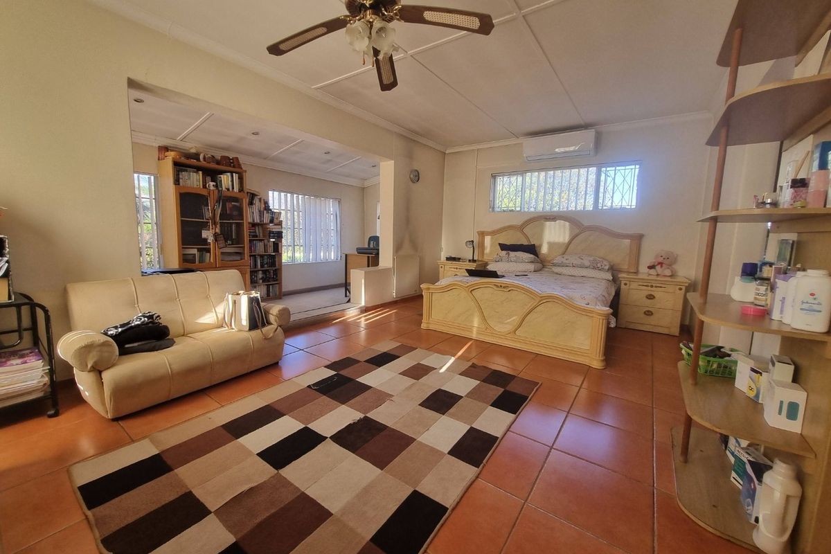 Spacious bedroom featuring tiled flooring, a ceiling fan, and a wall-mounted air conditioning unit, with an adjoining alcove area.