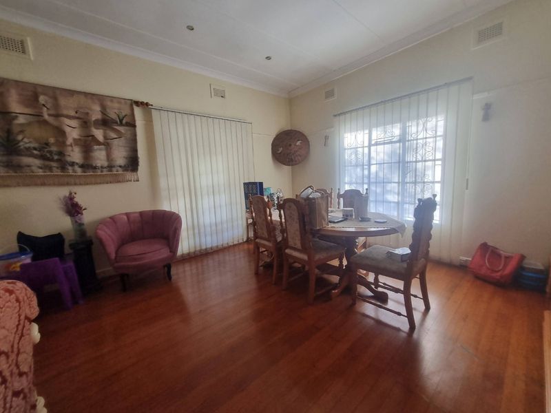 A dining room featuring polished hardwood flooring, large windows with security bars, and vertical blinds, providing a functional space for family meals.