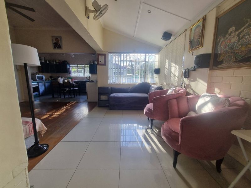 Open plan living area featuring a combination of tiled and timber flooring, vaulted ceilings, and a connected kitchen space with built-in cabinetry.