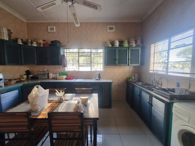 A functional kitchen featuring dated cabinetry, tiled splashbacks, double basin sink, and tiled flooring, offering potential for a modern renovation.