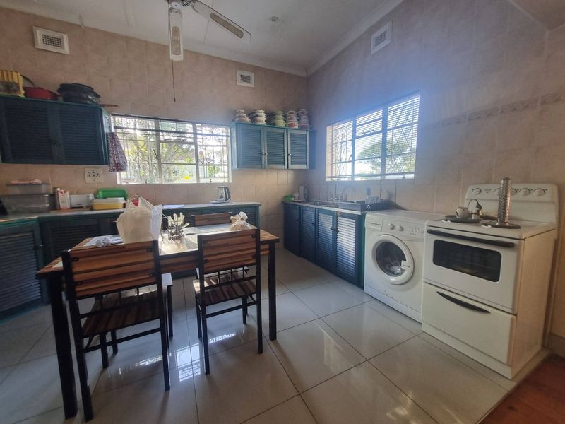 A functional kitchen featuring tiled walls and floors, built-in cabinetry, a double sink, and a freestanding stove with security bars on the windows.