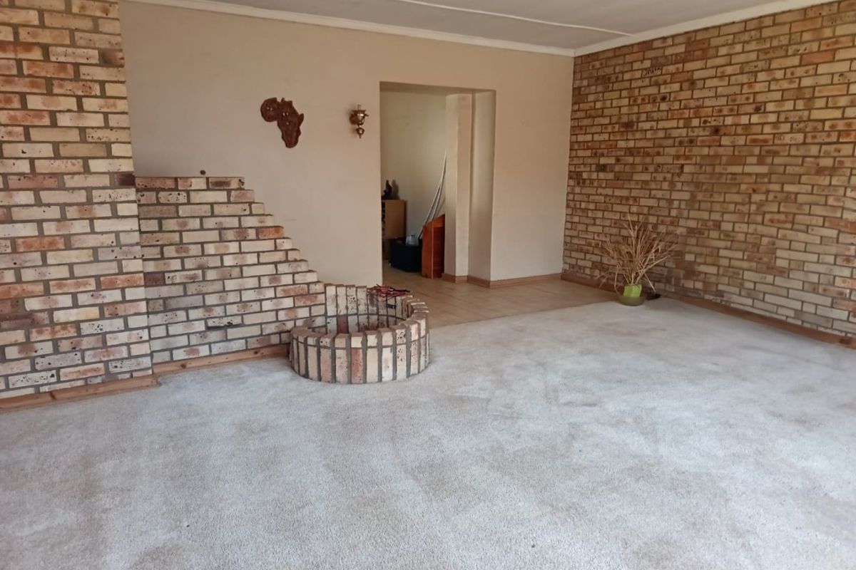 Spacious living area featuring a prominent brick fireplace and an exposed brick feature wall, offering a blank canvas for renovation.