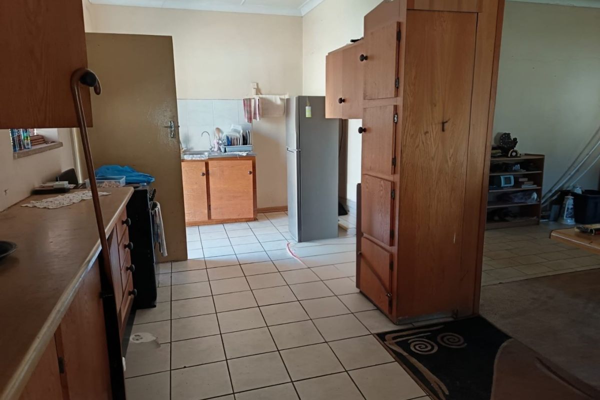 A dated kitchen featuring original wooden cabinetry, tiled flooring, and a functional sink area, offering significant potential for a modern renovation.