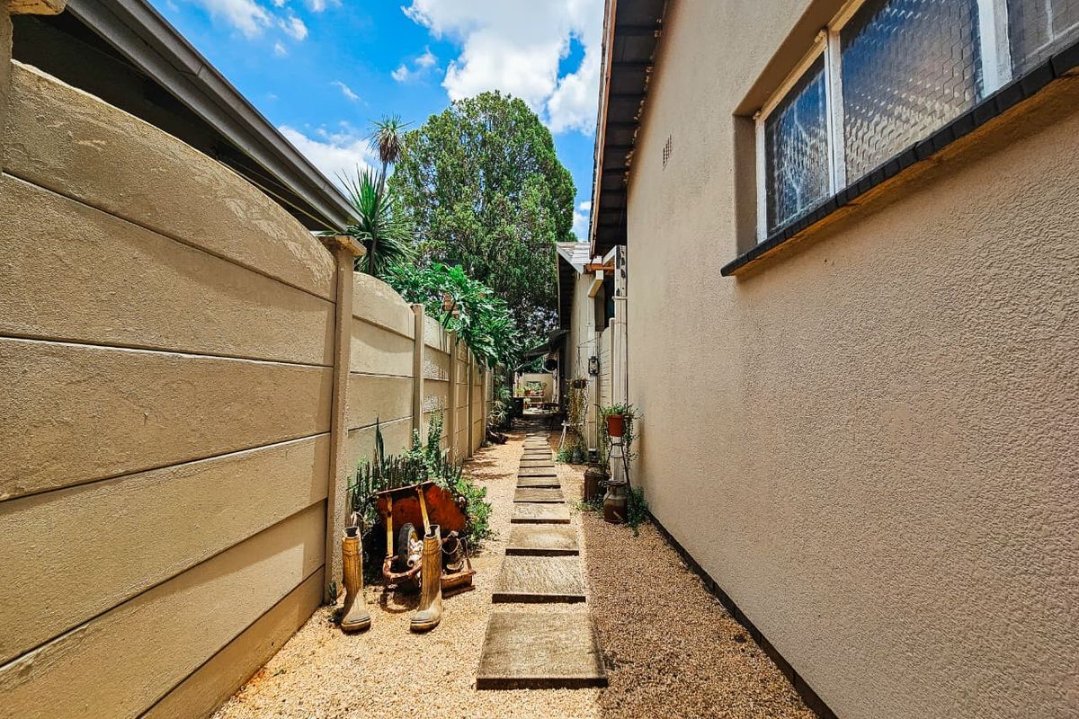 A narrow side passage featuring a gravel pathway with concrete pavers, bordered by a precast concrete boundary wall and the side elevation of the house.