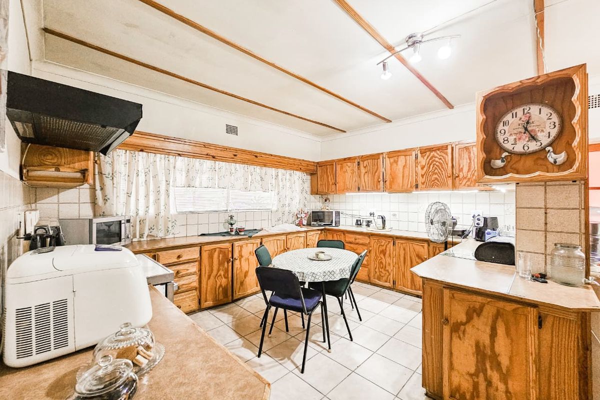 A dated kitchen featuring extensive wooden cabinetry, tiled flooring, and a tiled backsplash, offering a functional layout with significant potential for modern renovation.