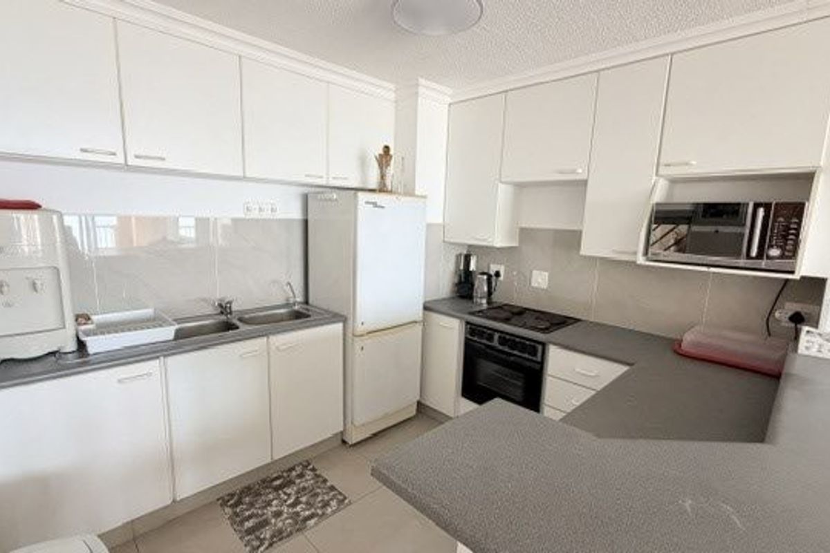 Functional kitchen featuring white built-in cabinetry, laminate countertops, integrated oven, electric hob, and a stainless steel double sink with tiled backsplash.