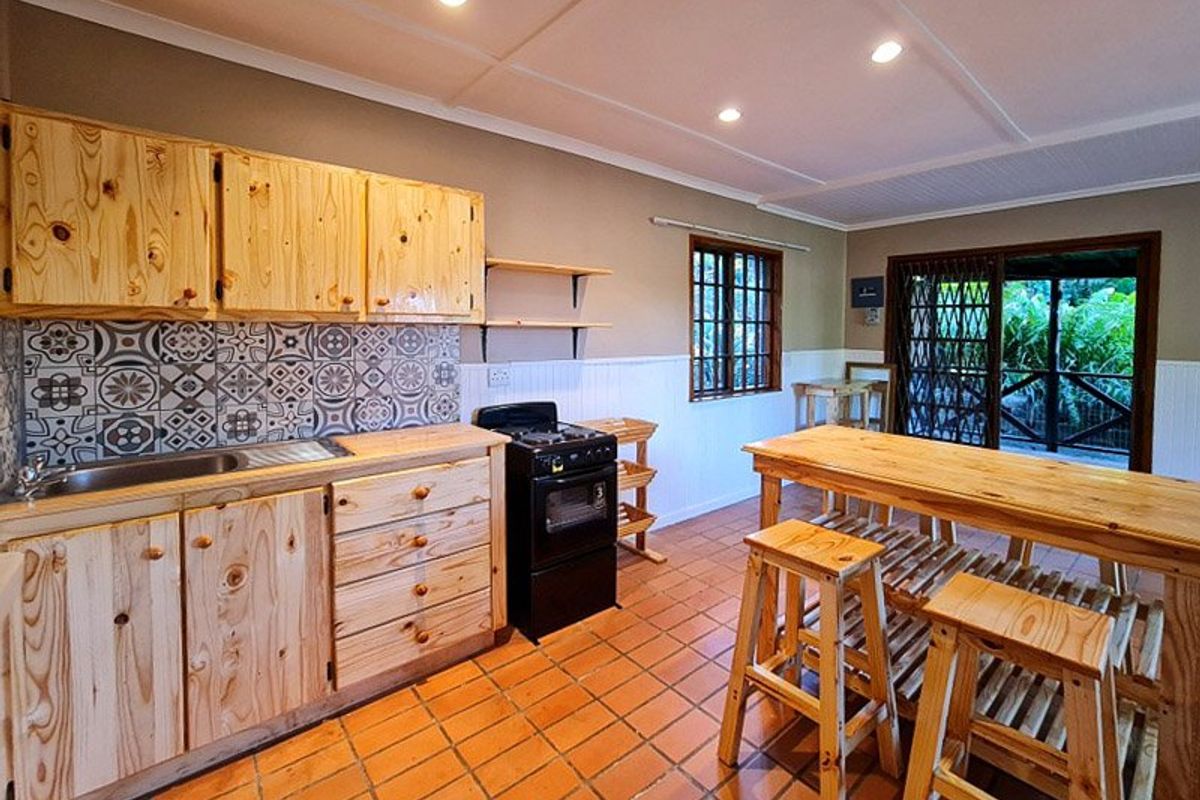 A rustic-style kitchen featuring natural wood cabinetry, patterned tile backsplash, terracotta flooring, and direct access to an outdoor patio area.
