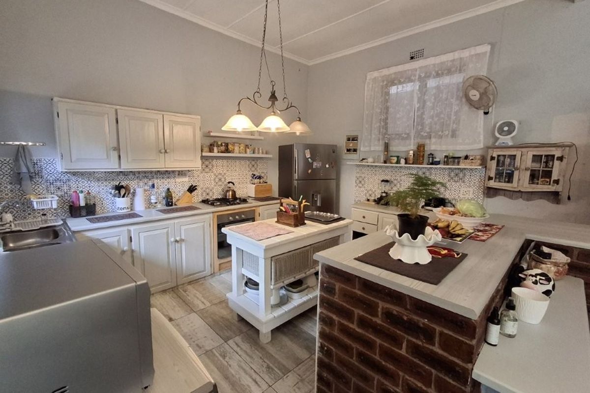 A functional kitchen featuring white cabinetry, a patterned tile backsplash, an exposed brick breakfast bar, and tiled flooring with integrated cooking appliances.