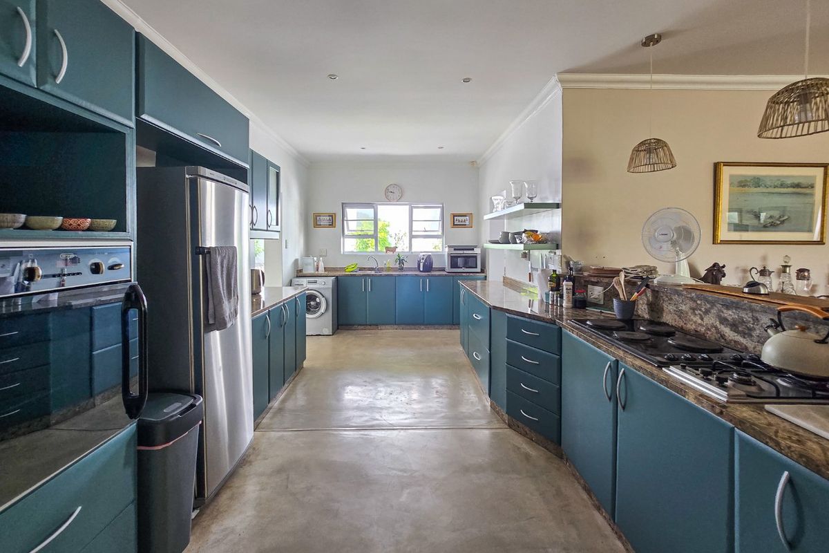 Spacious kitchen featuring teal cabinetry, stone countertops, integrated gas hob, built-in oven, and polished concrete flooring with a dedicated laundry area.