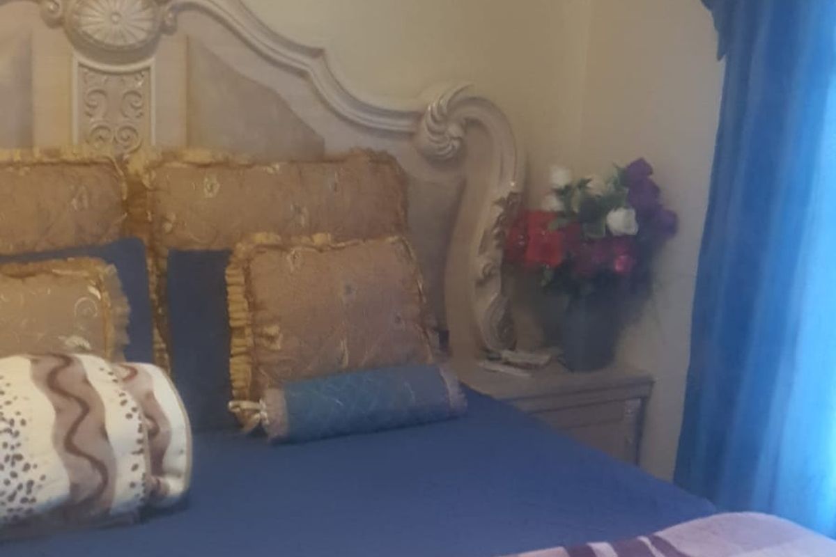 A bedroom featuring a large ornate headboard and window treatments.
