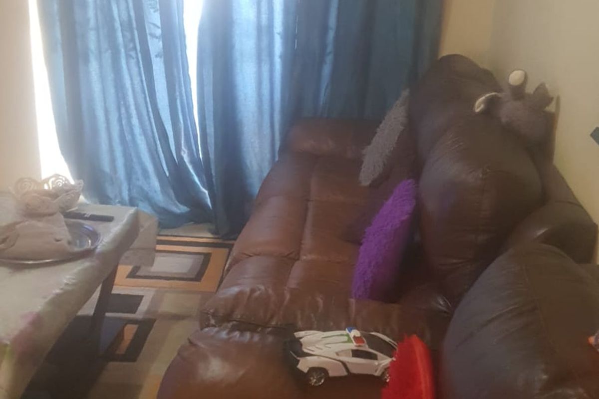 A living room area featuring a large sofa positioned near a window with curtains.