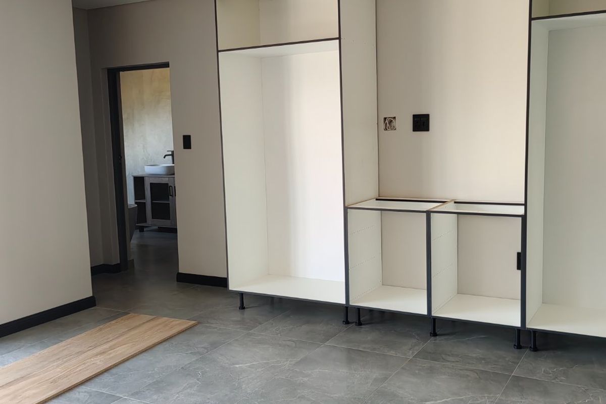 An unfinished kitchen space featuring modern grey floor tiles and partially installed built-in cabinetry, awaiting final completion and hardware.