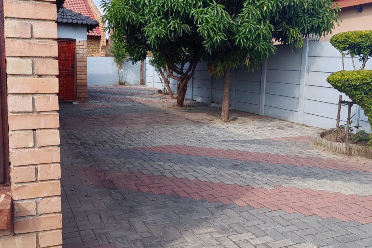 A paved side yard area featuring brick walling, mature trees, and a secure perimeter boundary wall.