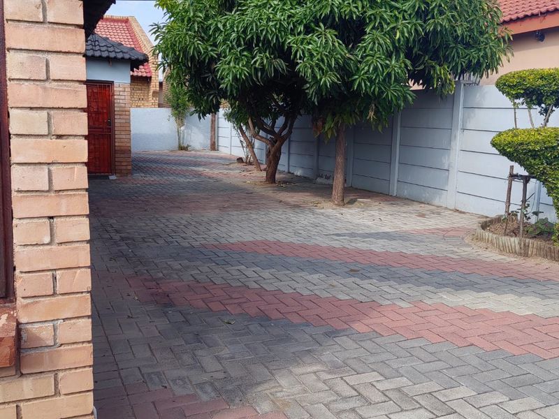 A paved side yard area featuring brick walling, mature trees, and a secure perimeter boundary wall.