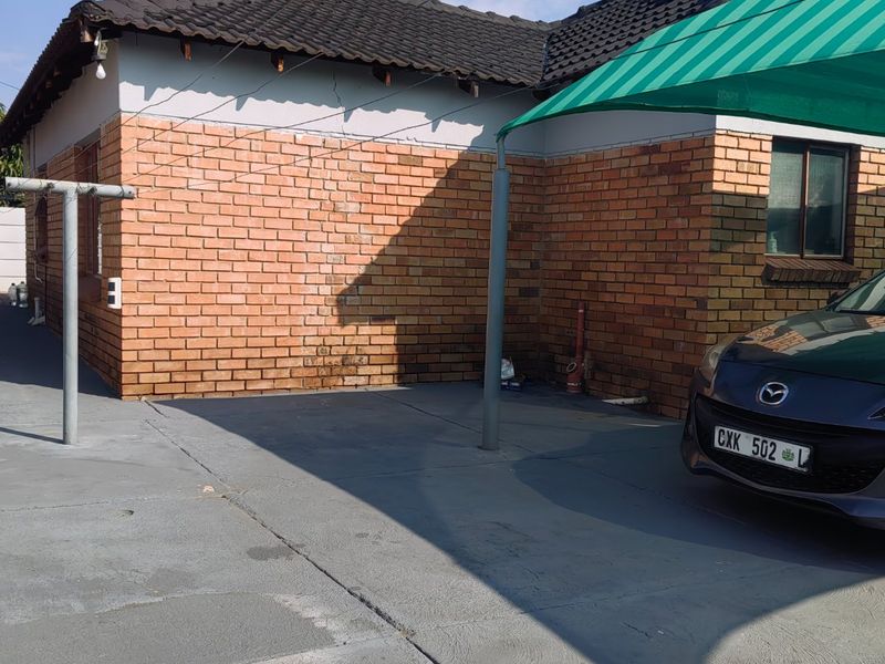 Exterior view of a face brick house featuring a tiled roof, a paved driveway, and a covered carport area.