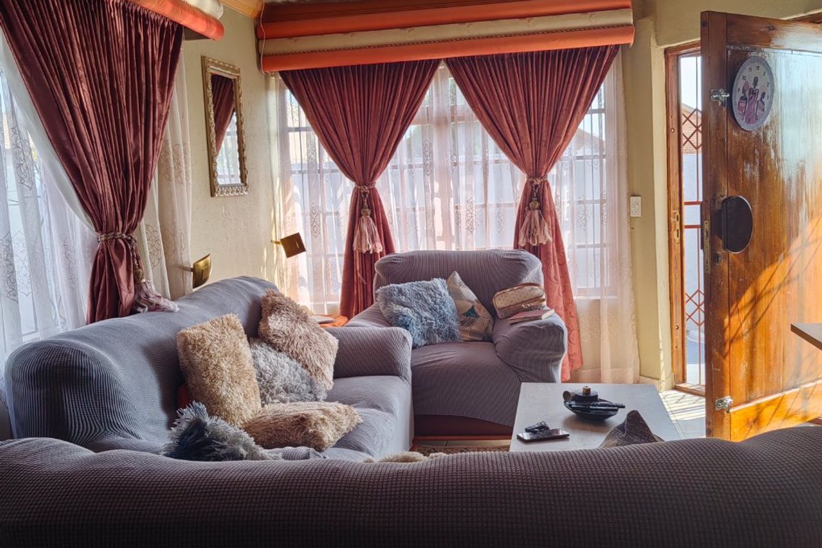 A cozy living room featuring decorative tin ceiling tiles, an ornate light fixture, and natural light streaming through large windows.