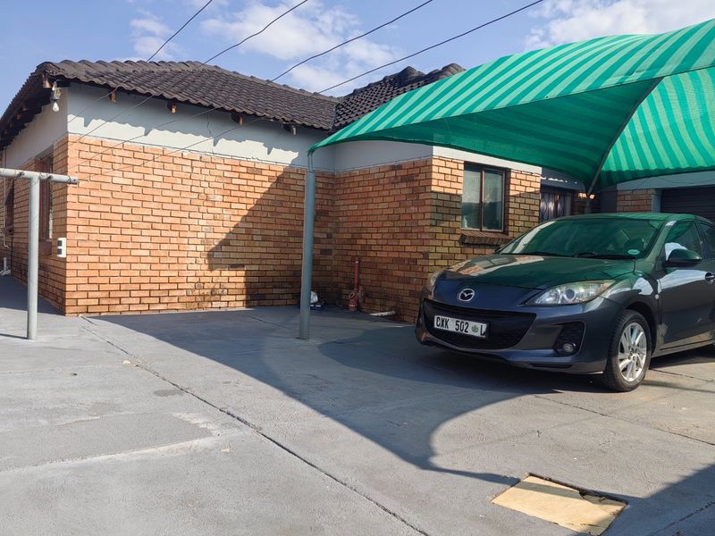 Front exterior view of the house featuring a face brick facade, concrete driveway, and a green shade cloth carport structure.