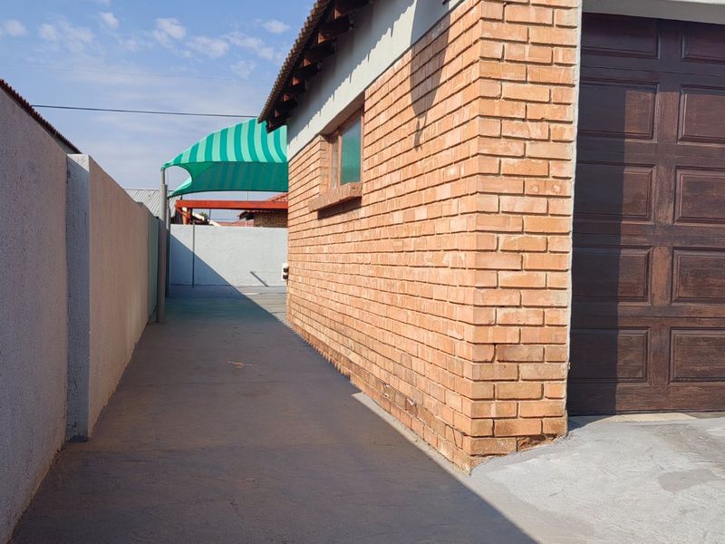 Side view of the property showing a brick exterior wall, garage door, and concrete driveway leading to a rear outdoor area.
