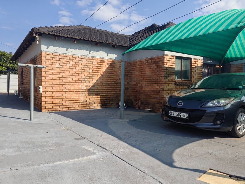 Front exterior view of the house featuring a face brick facade, concrete driveway, and a green shade cloth carport structure.