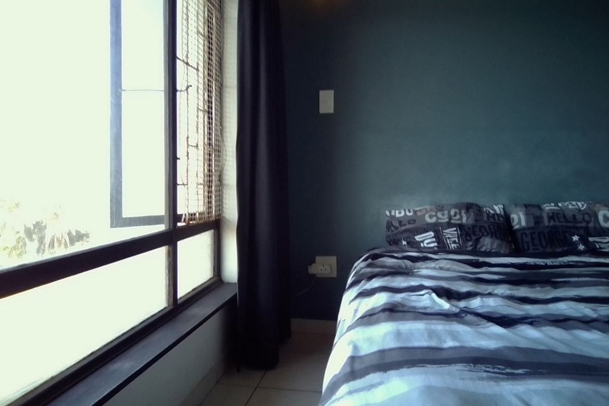 A bedroom featuring dark-toned walls, tiled flooring, and a large window with security bars, providing natural light.