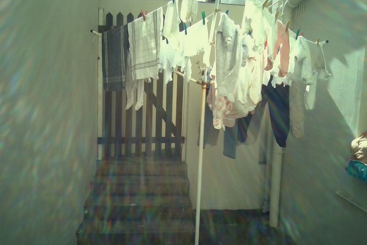 A small exterior utility area featuring concrete steps and a wooden gate, currently utilized for laundry drying.