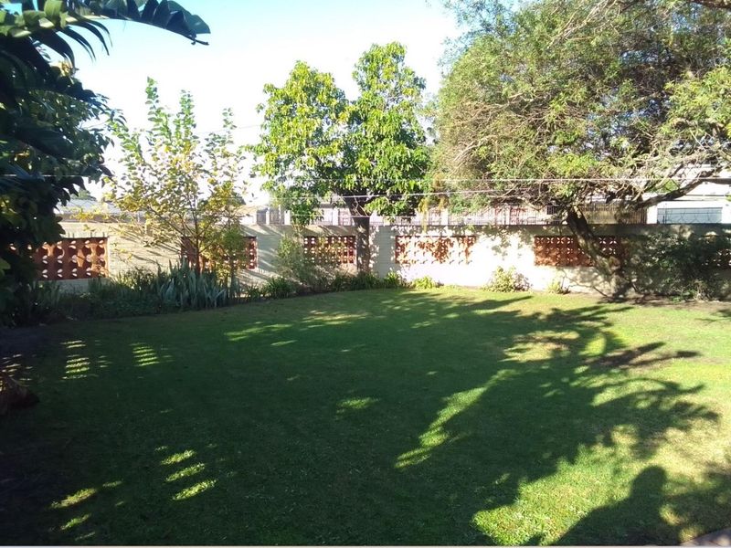 A private rear garden featuring a well-maintained lawn and a perimeter wall with decorative breeze block detailing.