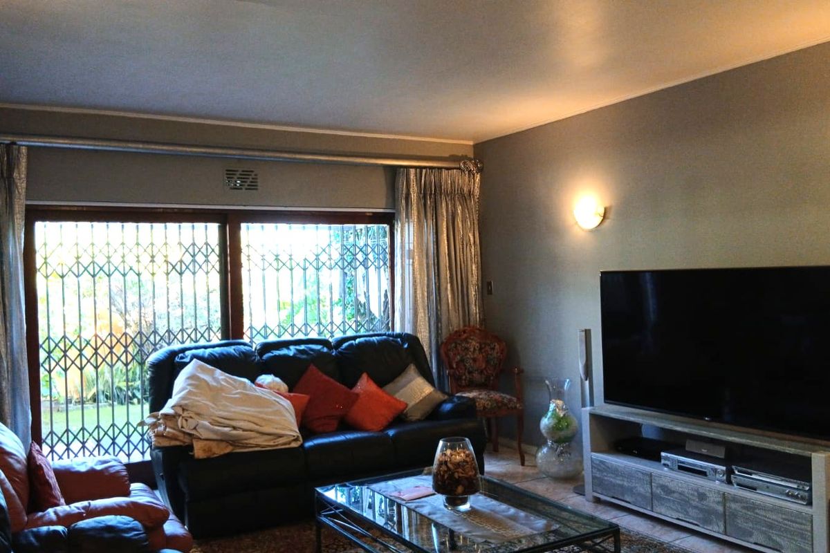 A comfortable living room featuring tiled flooring, wall sconce lighting, and a large sliding glass door with an integrated security gate.