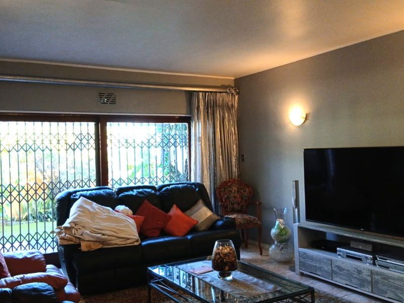 A comfortable living room featuring tiled flooring, wall sconce lighting, and a large sliding glass door with an integrated security gate.