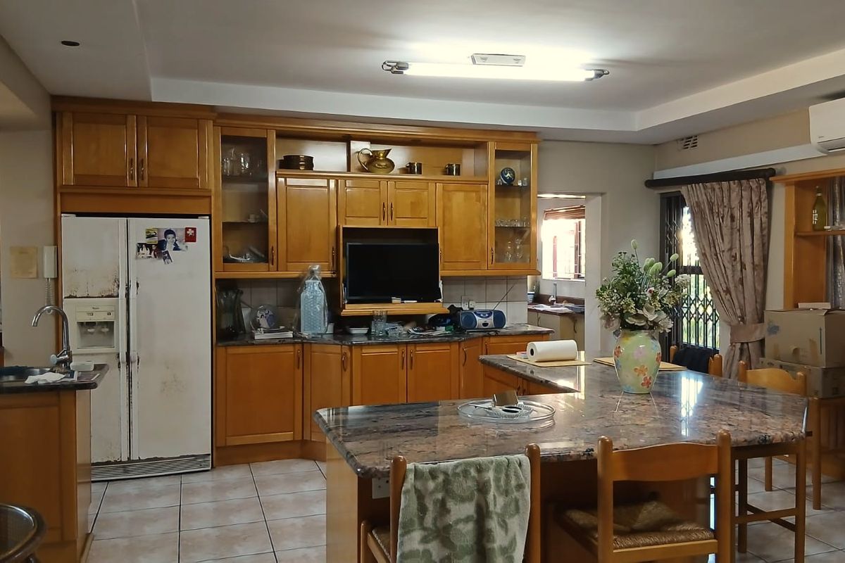 Spacious kitchen featuring extensive wooden cabinetry, granite countertops, a central island, and tiled flooring, offering a functional layout with potential for modern updates.