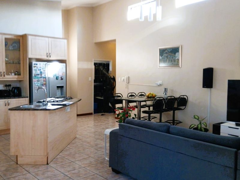 Open-plan living area featuring a functional kitchen with light wood cabinetry, a central island, and tiled flooring throughout the combined space.