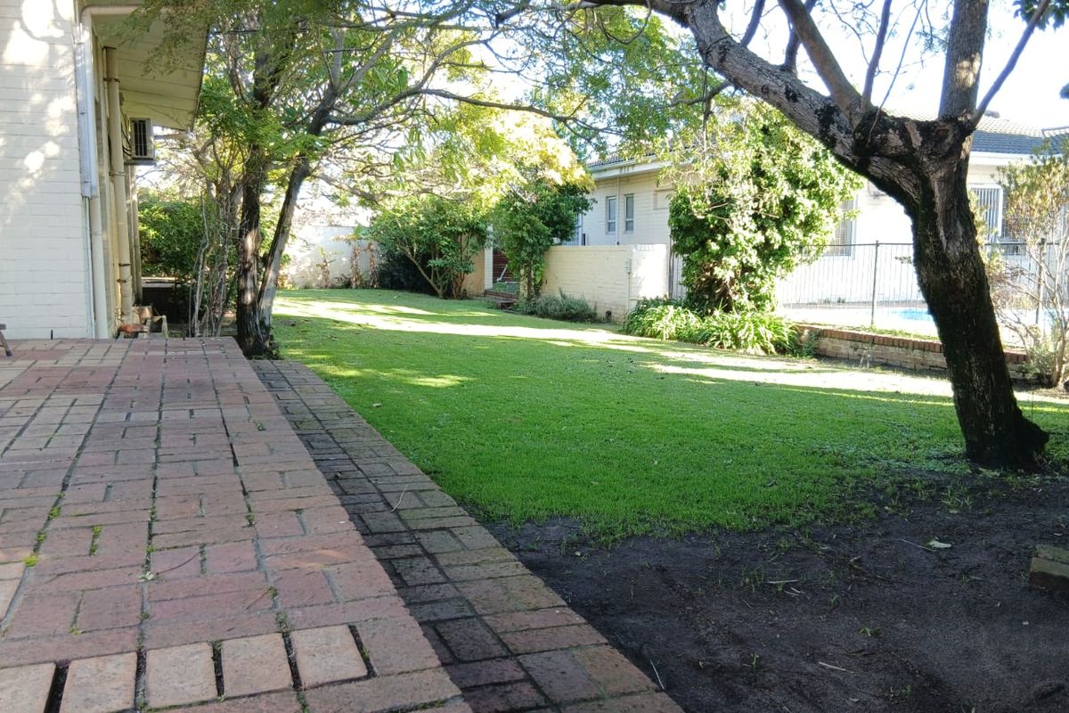 A spacious rear garden featuring a brick-paved patio area, established trees, and a lawn leading to a rear boundary fence.