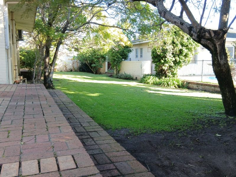 A spacious rear garden featuring a brick-paved patio area, established trees, and a lawn leading to a rear boundary fence.