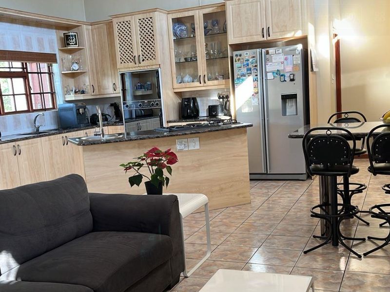 Open-plan kitchen and living area featuring light wood cabinetry, granite countertops, built-in appliances, and tiled flooring throughout.