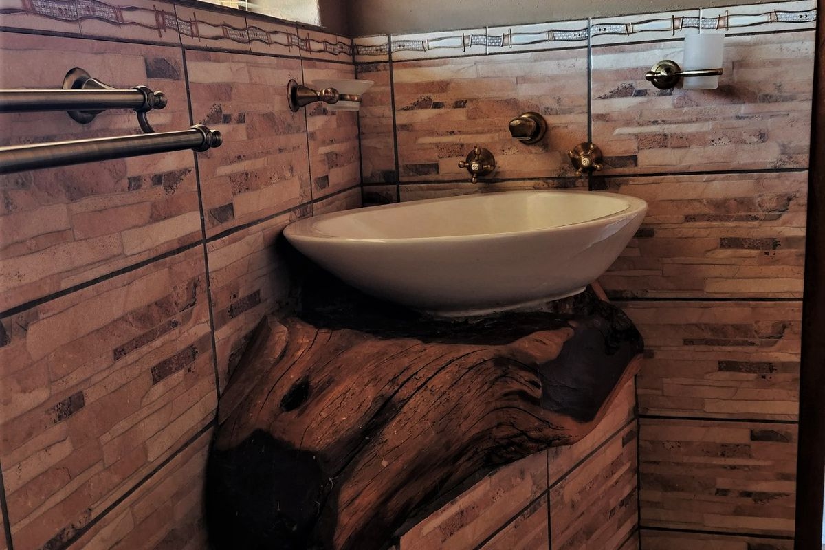 A rustic-style bathroom vanity featuring a white vessel sink mounted on a natural wood slab, complemented by brass fixtures and decorative wall tiling.
