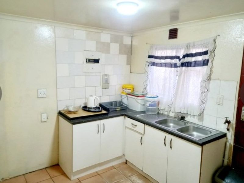 A compact kitchen featuring double bowl stainless steel sink, laminate countertops, tiled splashback, and built-in cabinetry with tiled flooring.