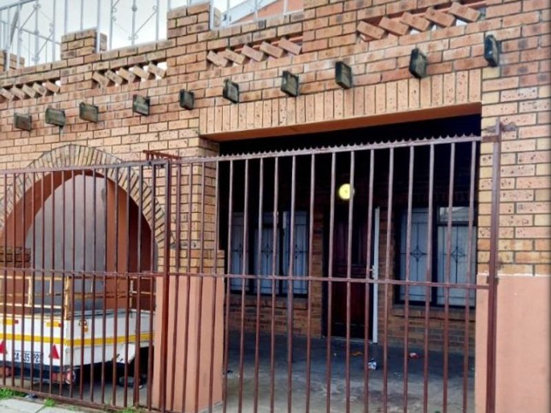 Front elevation of an apartment featuring a face brick facade, arched entryway, and secure metal gate enclosure.