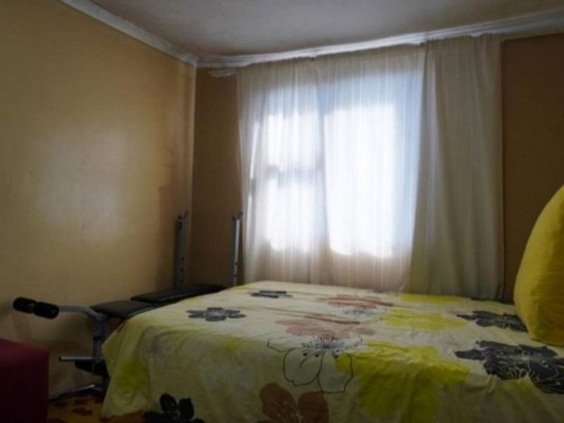 A bedroom featuring standard wall finishes and a window with curtains, requiring cosmetic updates to improve its overall appeal.