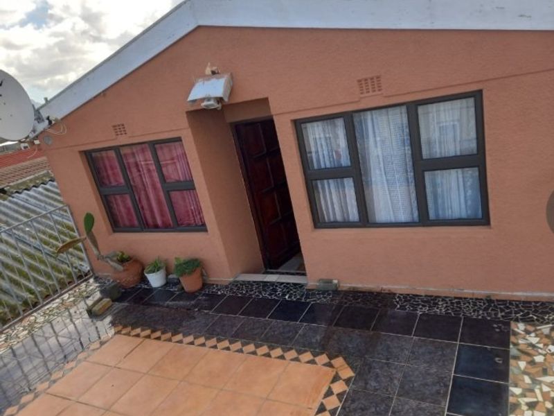 Front exterior view of the apartment featuring a tiled patio area, aluminium window frames, and a timber entrance door.