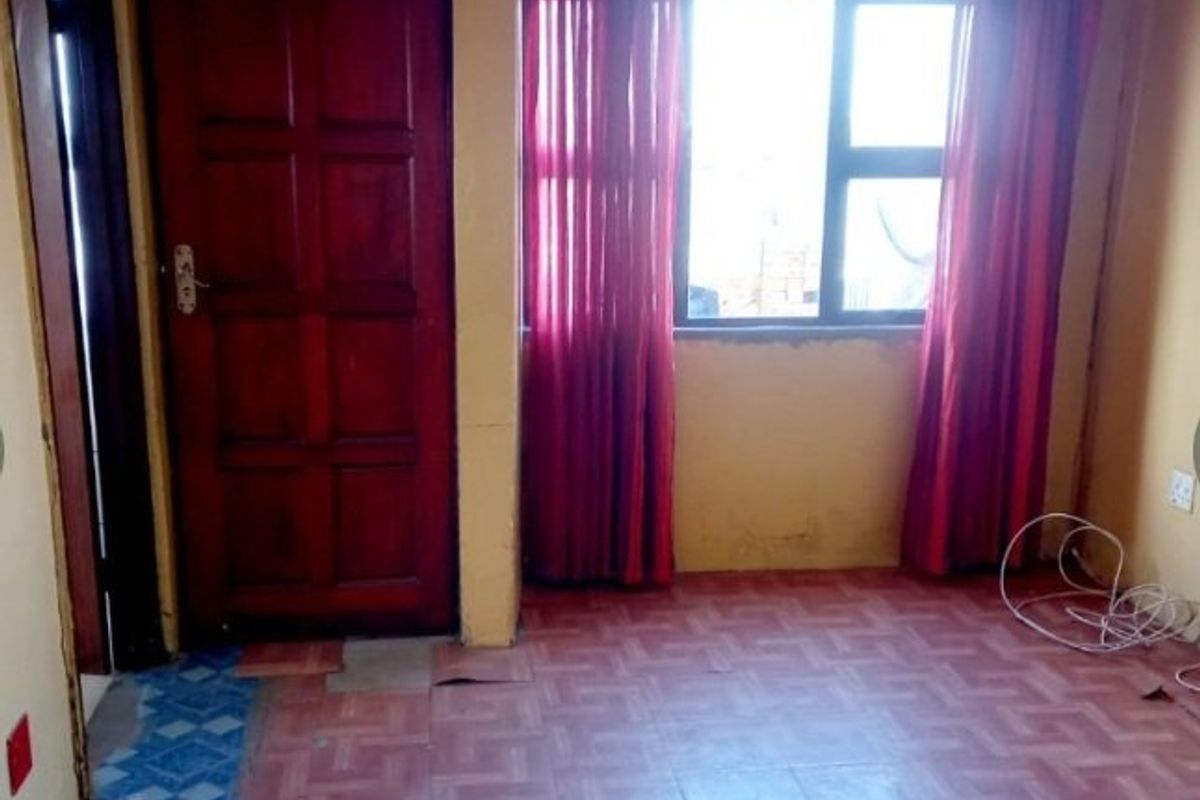An empty bedroom featuring tiled flooring, a timber door, and an aluminium window frame, requiring cosmetic updates and floor repairs.