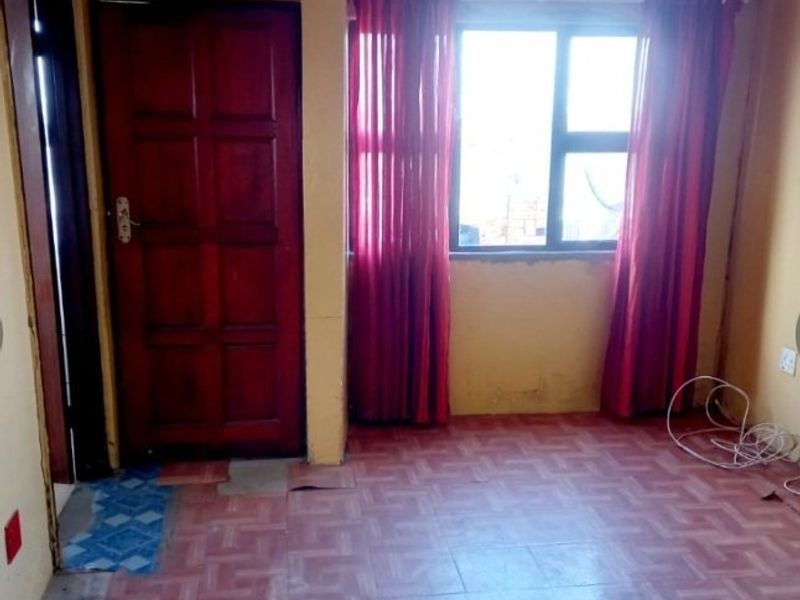 An empty bedroom featuring tiled flooring, a timber door, and an aluminium window frame, requiring cosmetic updates and floor repairs.