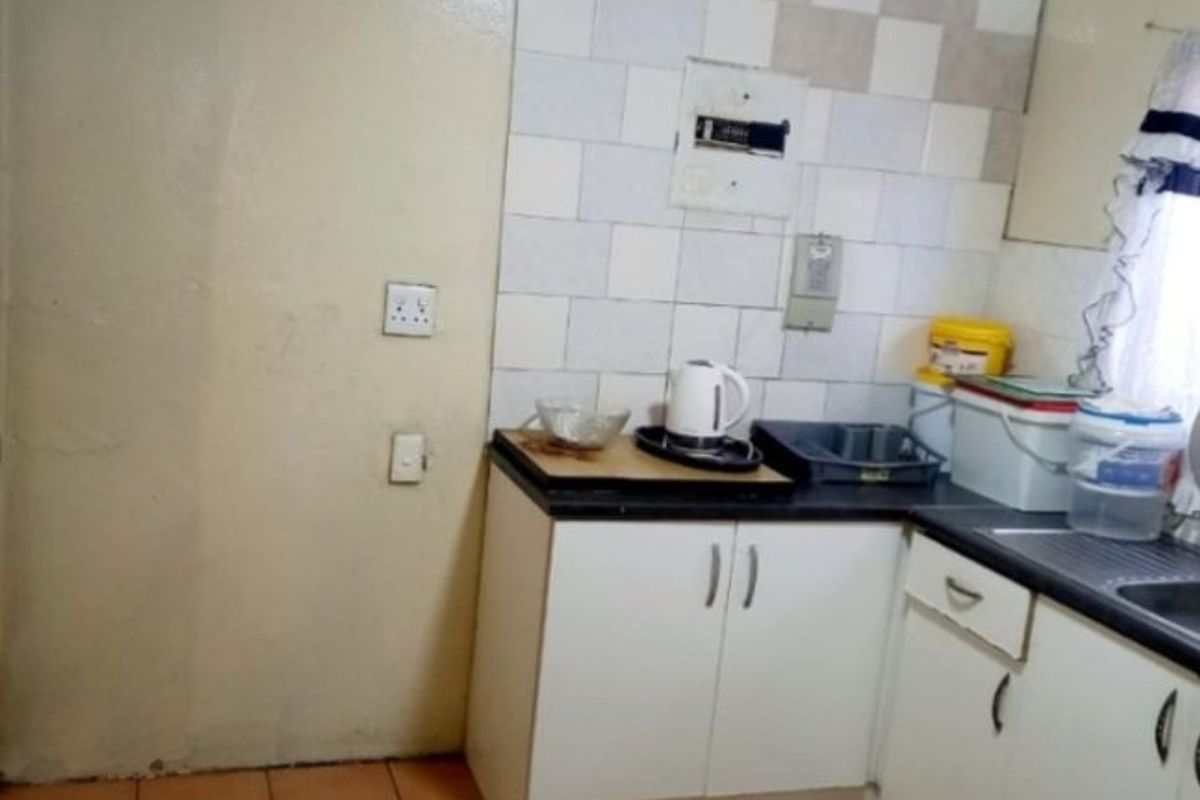 A compact kitchen featuring tiled flooring, built-in base cabinetry, laminate countertops, and a tiled splashback, offering a functional space in need of cosmetic updates.