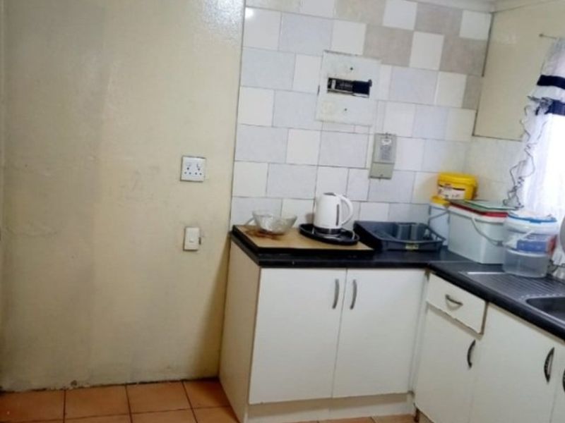 A compact kitchen featuring tiled flooring, built-in base cabinetry, laminate countertops, and a tiled splashback, offering a functional space in need of cosmetic updates.
