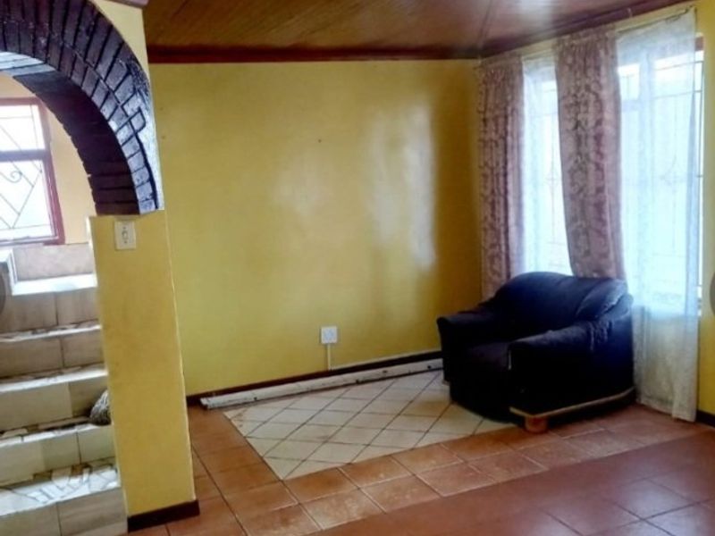 Living area featuring a distinctive timber-clad vaulted ceiling, brick archway detail, and ceramic tiled flooring with security bars on the windows.