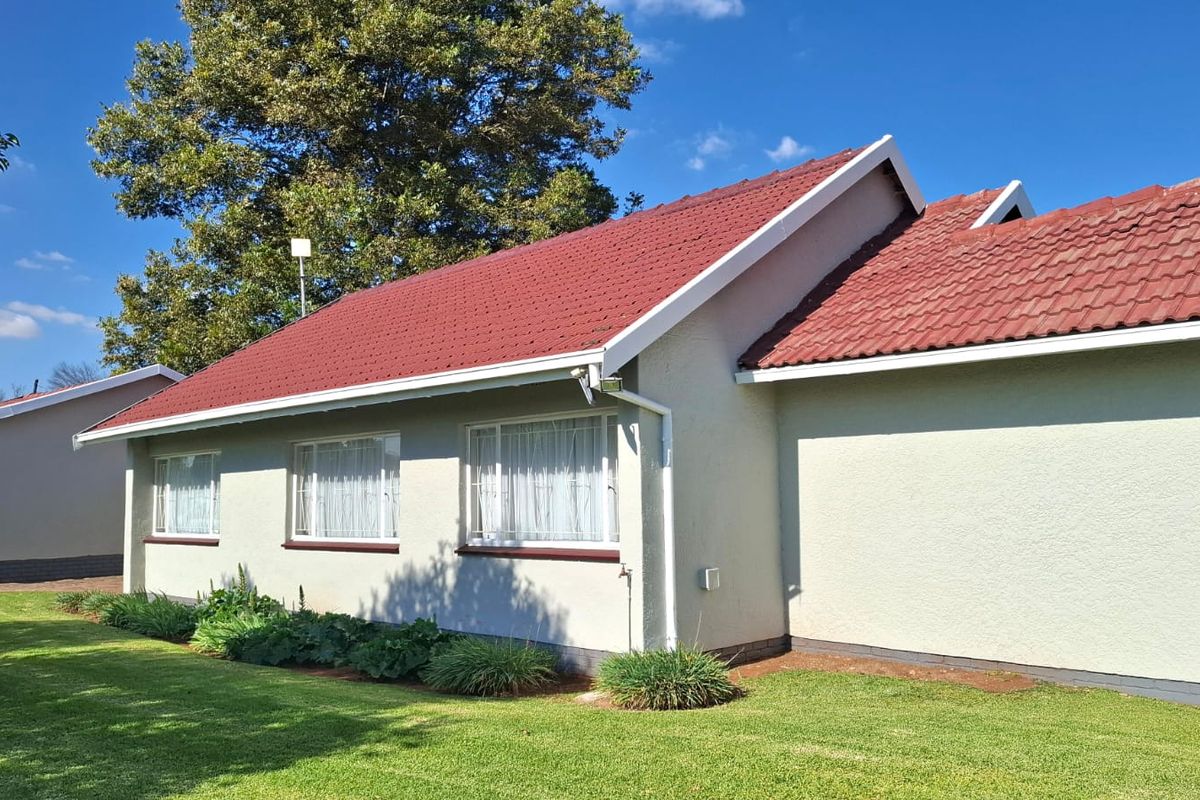 A well-maintained rear exterior view of the house featuring a red tiled roof, plastered walls, and a neat surrounding lawn.