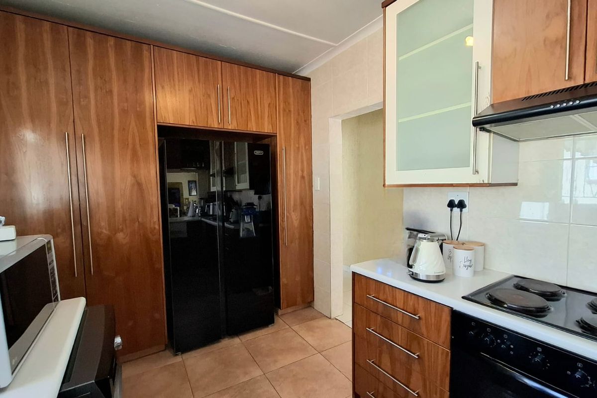 A functional kitchen featuring wood-finish cabinetry, a built-in oven and hob, extractor fan, and tiled flooring with a neutral backsplash.