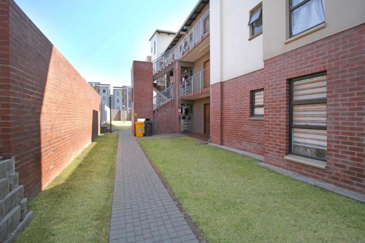 A view of the rear exterior of the apartment complex, featuring a paved walkway, lawn area, and multi-level access staircases.