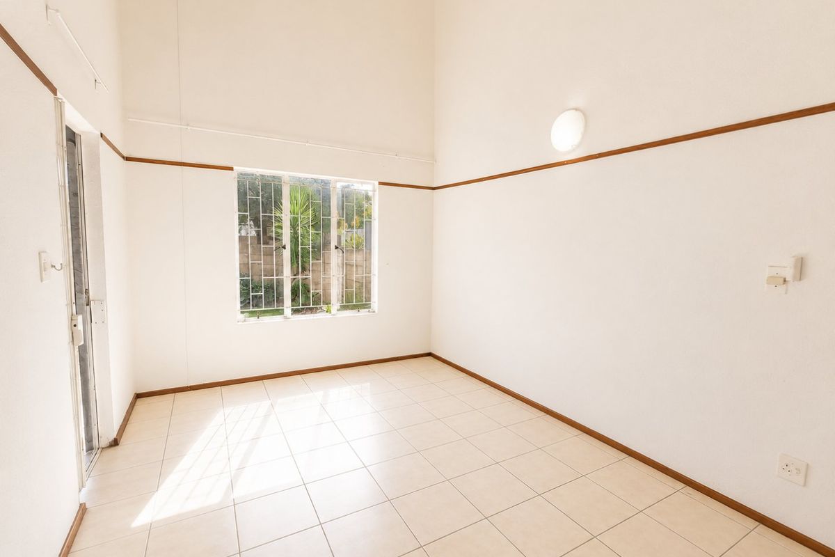 A bright, empty living area featuring high ceilings, neutral tiled flooring, and a window with security bars, offering a clean canvas for interior design.