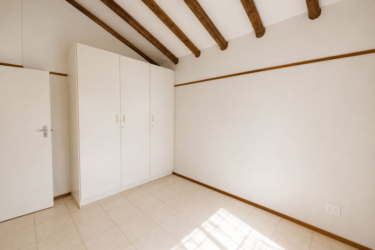 A bright, empty bedroom featuring exposed timber ceiling beams, tiled flooring, and a built-in wardrobe.