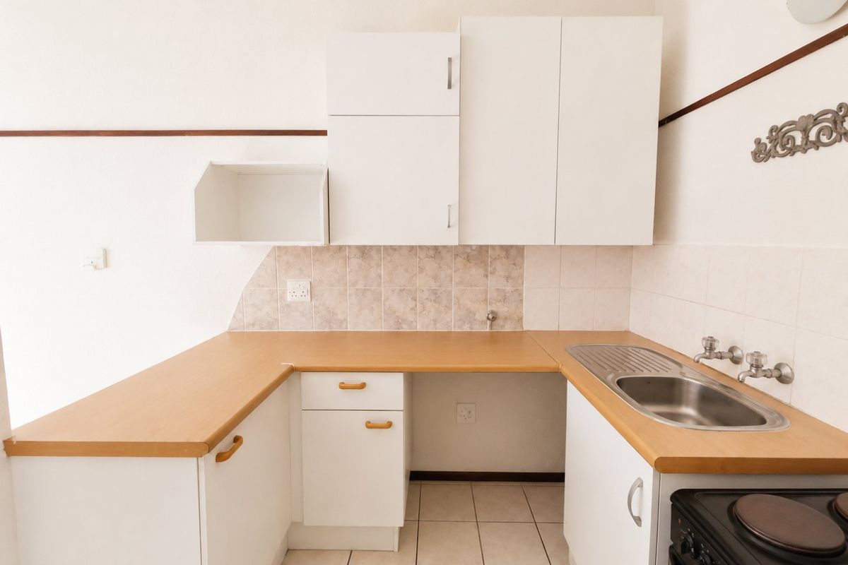 A functional kitchen featuring laminate countertops, stainless steel sink, wall-mounted cabinetry, and tiled splashback, providing a clean and practical workspace.